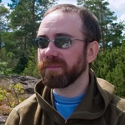 Alex Stein outdoors, in sunglasses, with pine trees behind